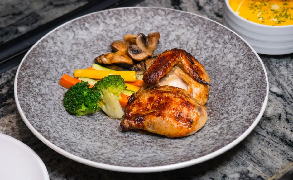 Plate of roasted chicken served with colorful vegetables in an elegant setting.