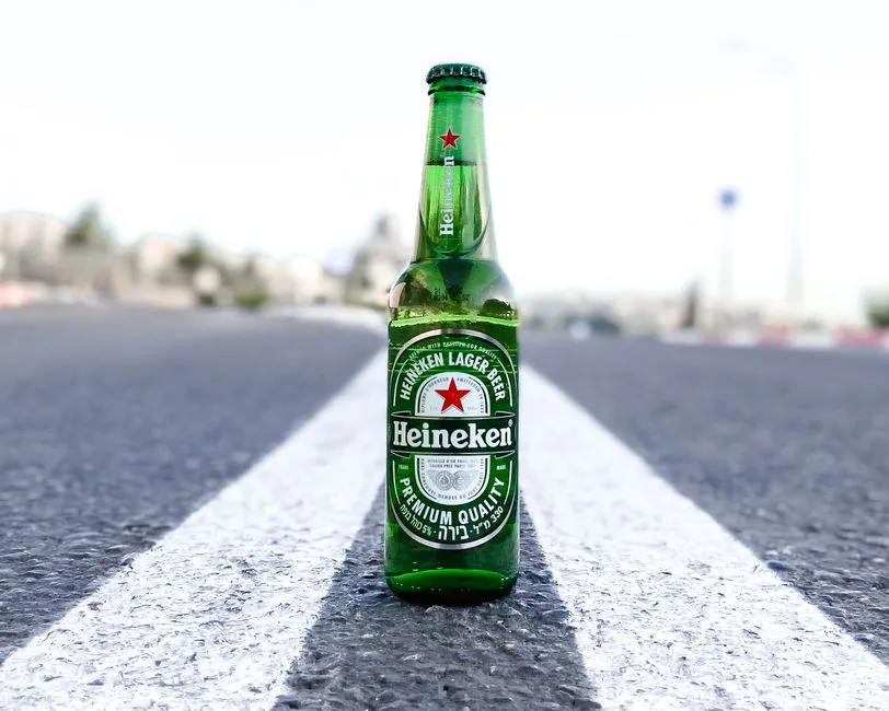 Close-up of a Heineken beer bottle placed on the middle of an urban road.
