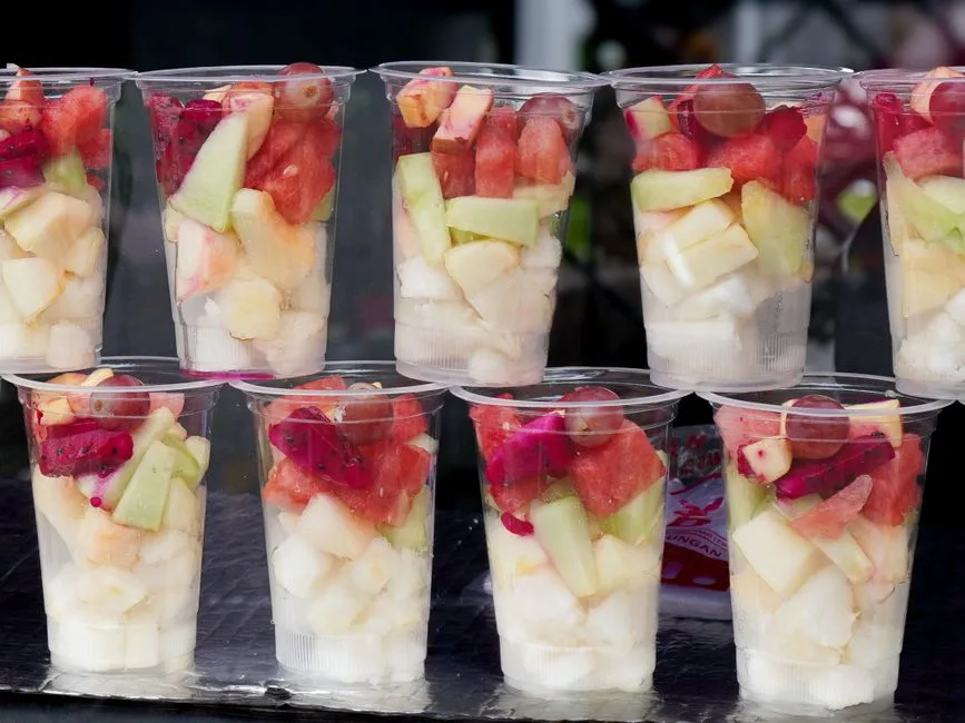 A selection of colorful fruit cups with chopped melons, dragon fruit, and grapes showcased beautifully in clear containers.
