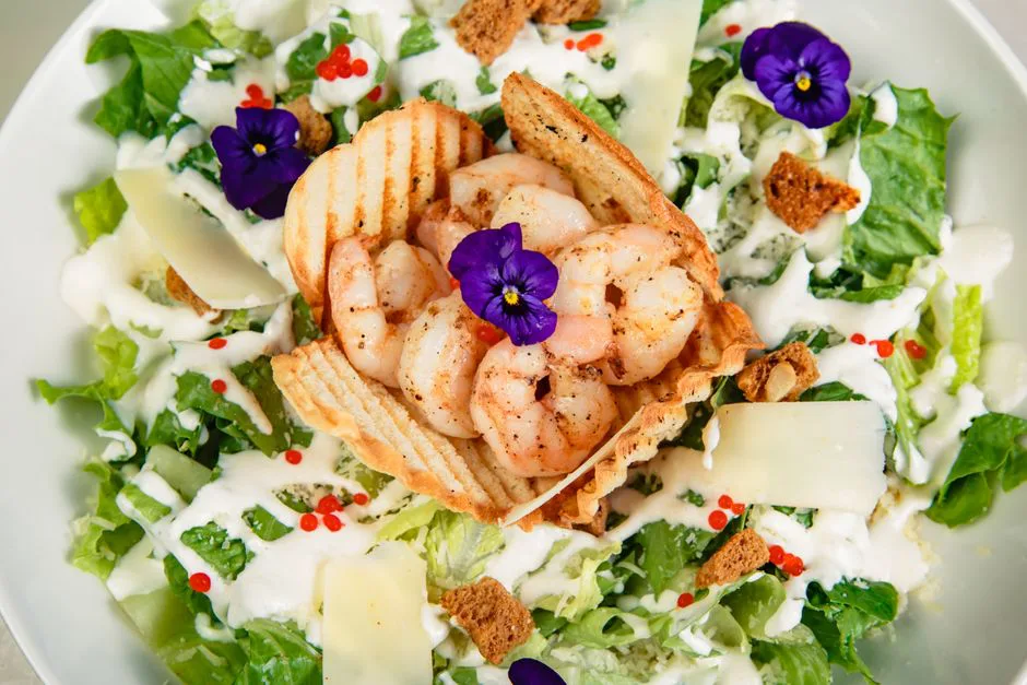 Fresh shrimp Caesar salad garnished with edible flowers and creamy dressing.