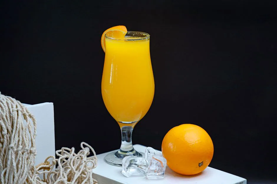 Fresh orange juice served in a glass with ice and a whole orange on a black background.