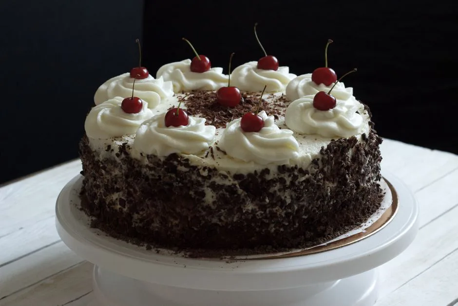 Delicious Black Forest cake topped with whipped cream and cherries on a cake stand.