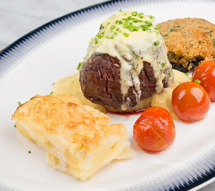 Elegant steak dish with layered potatoes, cherry tomatoes, and creamy sauce on a stylish plate.