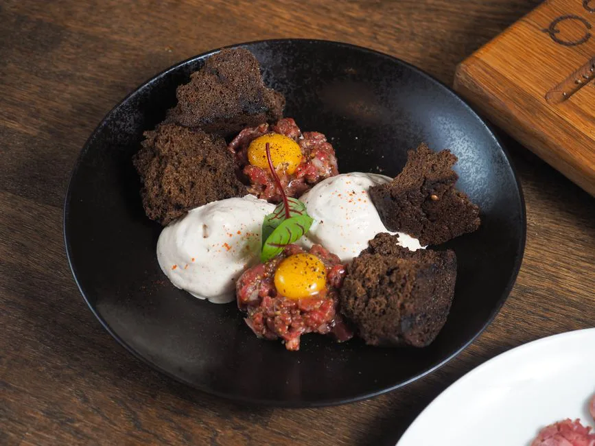 Savor the flavors of gourmet beef tartare topped with quail eggs, cream sauce, and rye bread cubes.