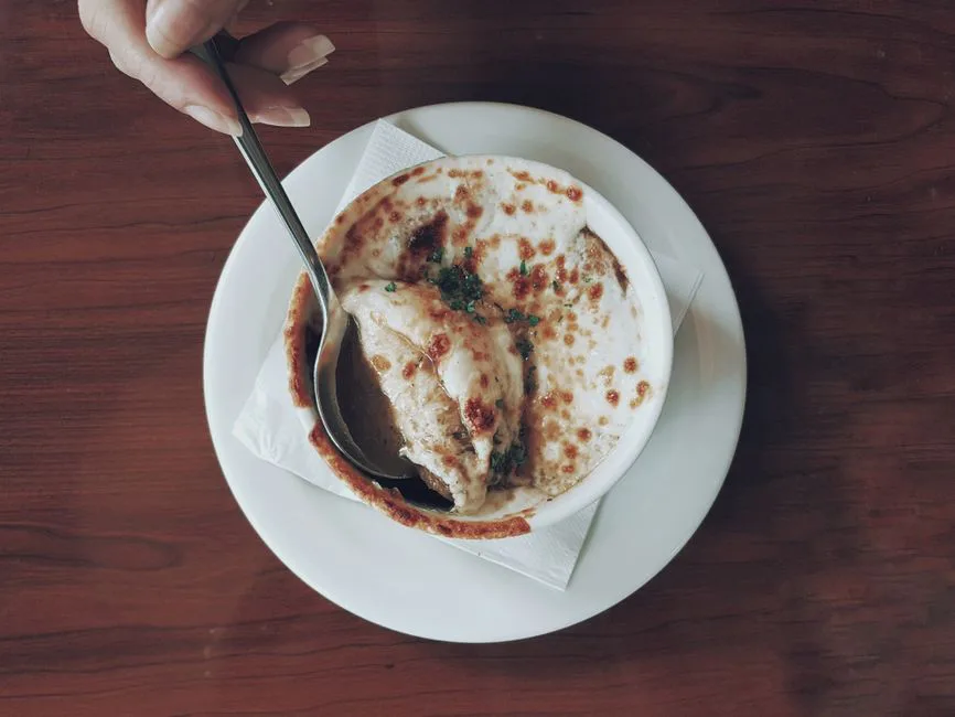 Top view of gourmet French onion soup with melted cheese in a ceramic bowl, served with a spoon.