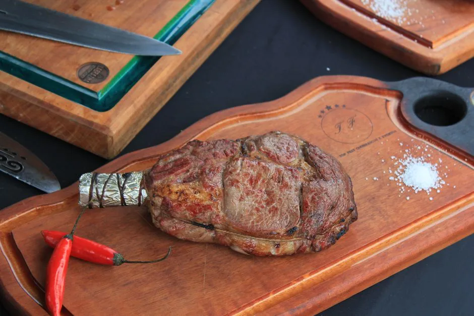 Delicious grilled ribeye steak on wooden board, garnished with chili peppers.