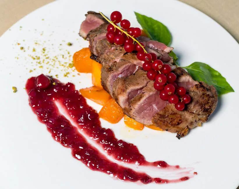 Sliced duck breast served with red currant sauce, enhancing a gourmet dining experience.