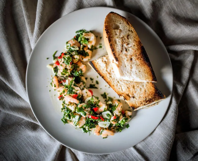 Top view of shrimp with herbs and toasted bread on a white plate.