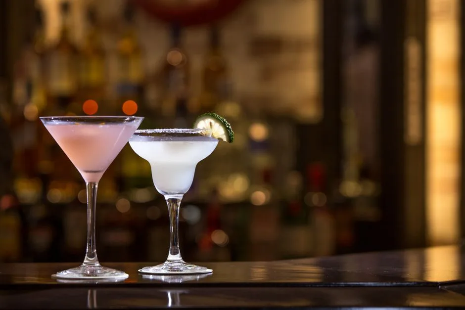 Two cocktails with lime garnish on a bar, set against a blurred background. Perfect for nightlife scenes.