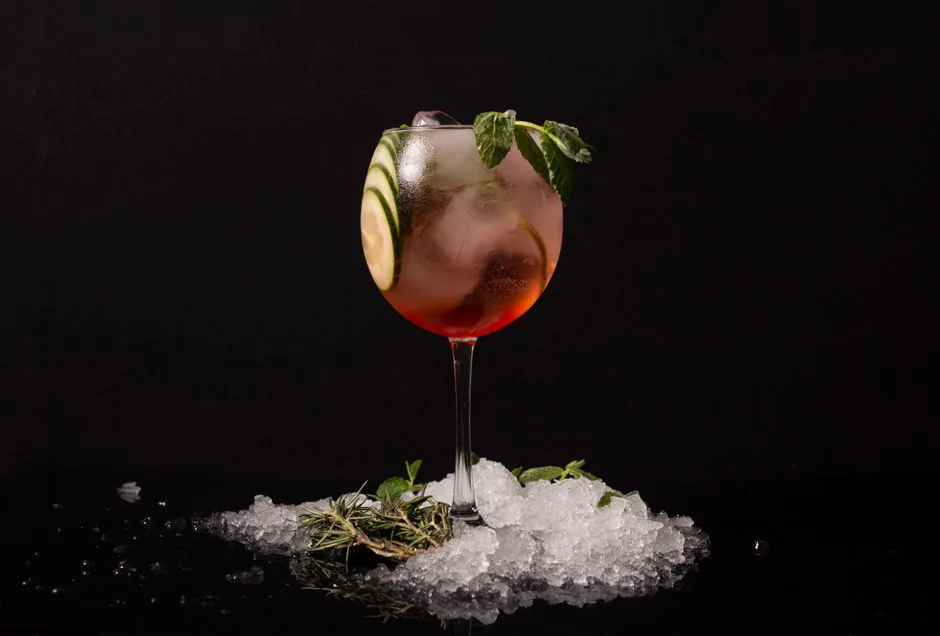 A refreshing cocktail in a glass with cucumber and mint garnish, surrounded by ice.