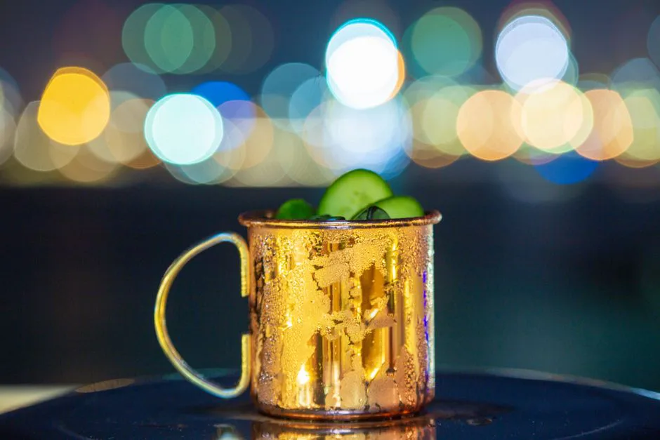 Close-up of a Moscow Mule in a copper mug with vibrant bokeh city lights in the background.