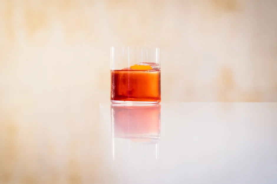 Elegant glass of Negroni with orange peel garnish on reflective surface, perfect for lifestyle and drink concepts.