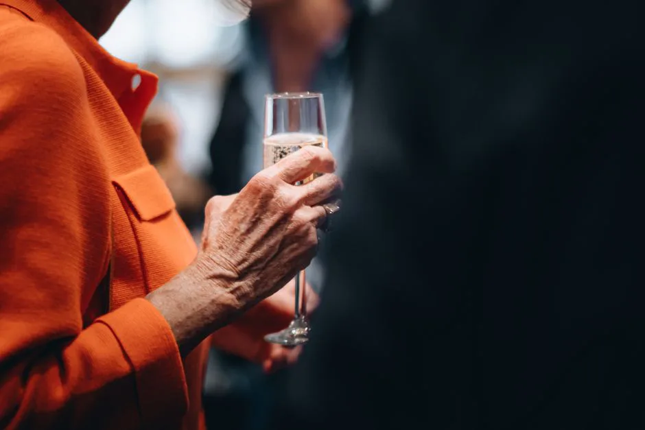 Close-up of a woman holding a champagne glass at a formal event, wearing an orange outfit.
