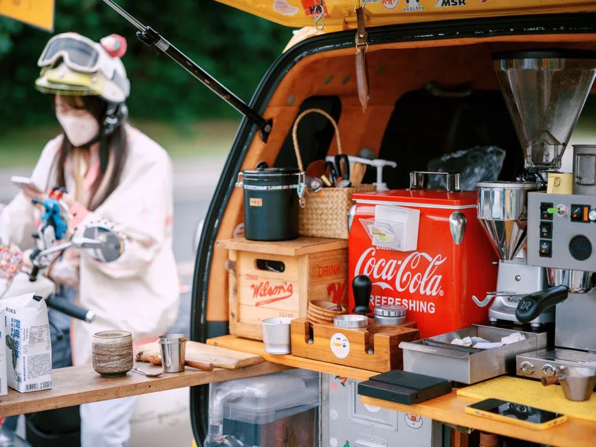 Colorful mobile coffee stand with equipment and a masked barista outdoors.