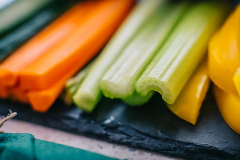 Vibrant mix of fresh carrot, celery, cucumber, and bell pepper sticks on slate board.