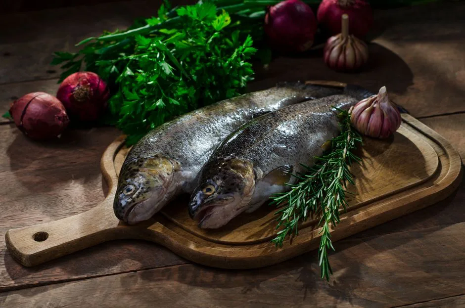Fresh whole fish on a wooden board with herbs and vegetables, perfect for culinary presentations.