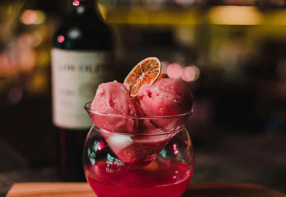 A refreshing pink sorbet with a citrus garnish in an elegant glass, perfect for dessert lovers.