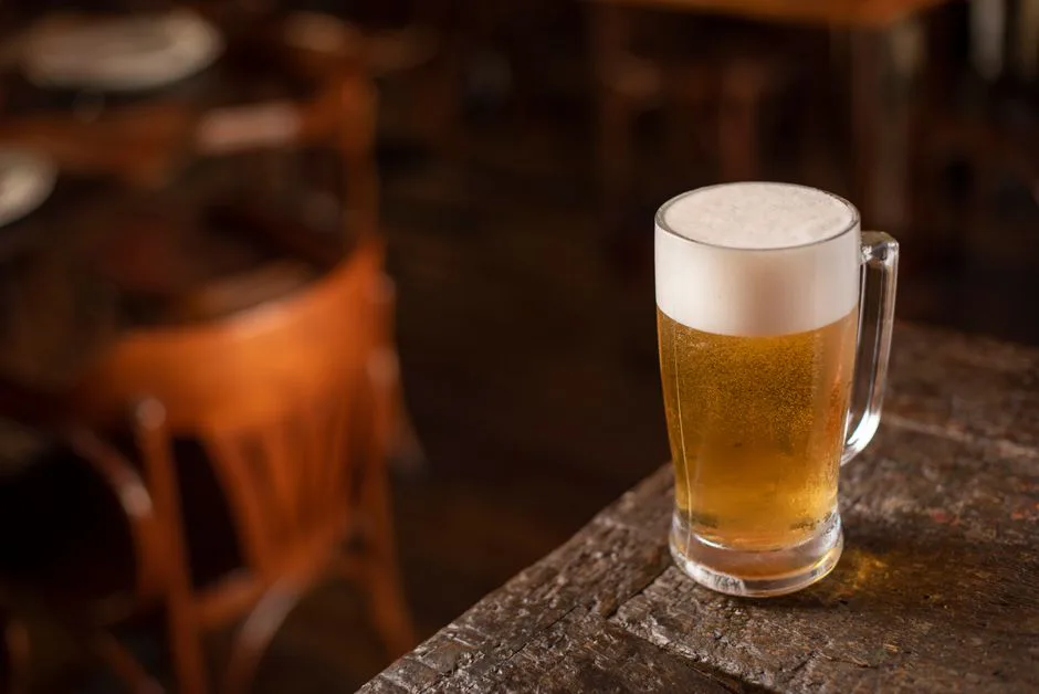 Close-up of a frothy beer mug on a wooden table in a cozy pub setting.