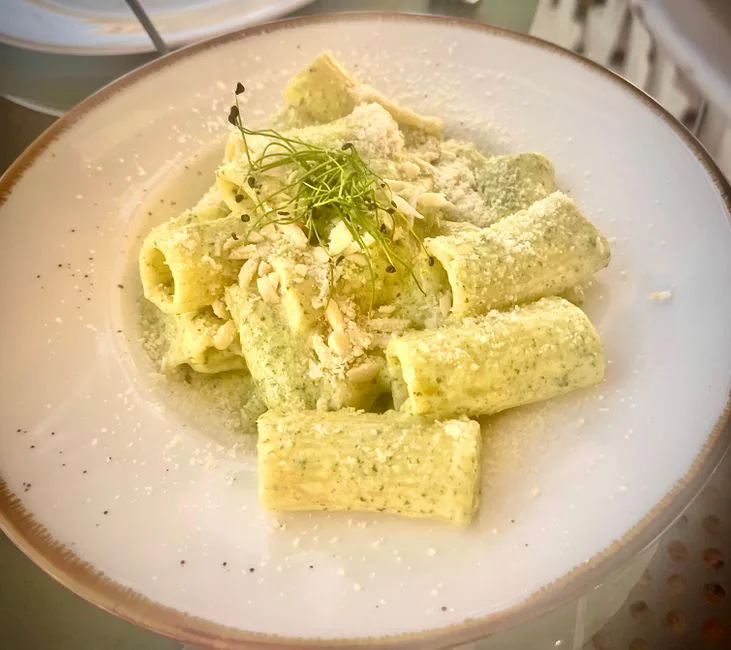 Delicious rigatoni pasta with creamy pesto sauce, garnished with cheese and microgreens, served on a white plate.