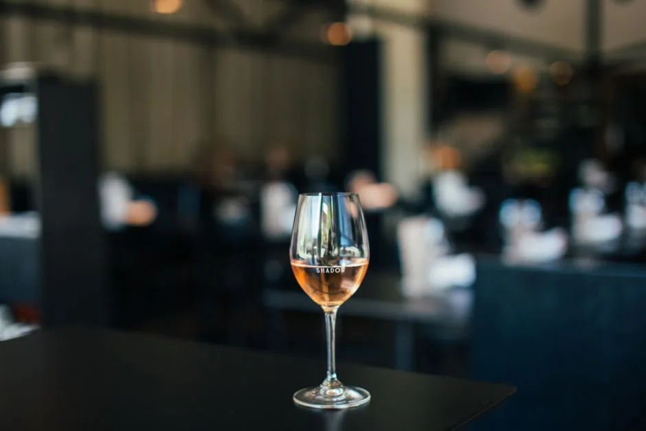 Glass goblet filled with tasty alcoholic drink placed on black table in modern restaurant with dark tables on blurred background
