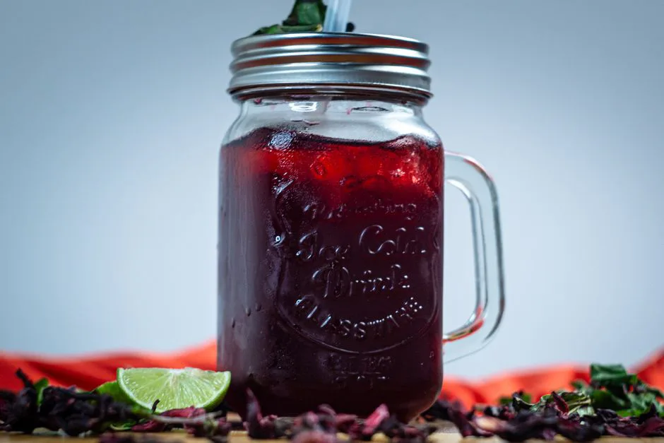 Chilled agua de jamaica served in a mason jar with mint leaves and lime slice, perfect for summer refreshment.