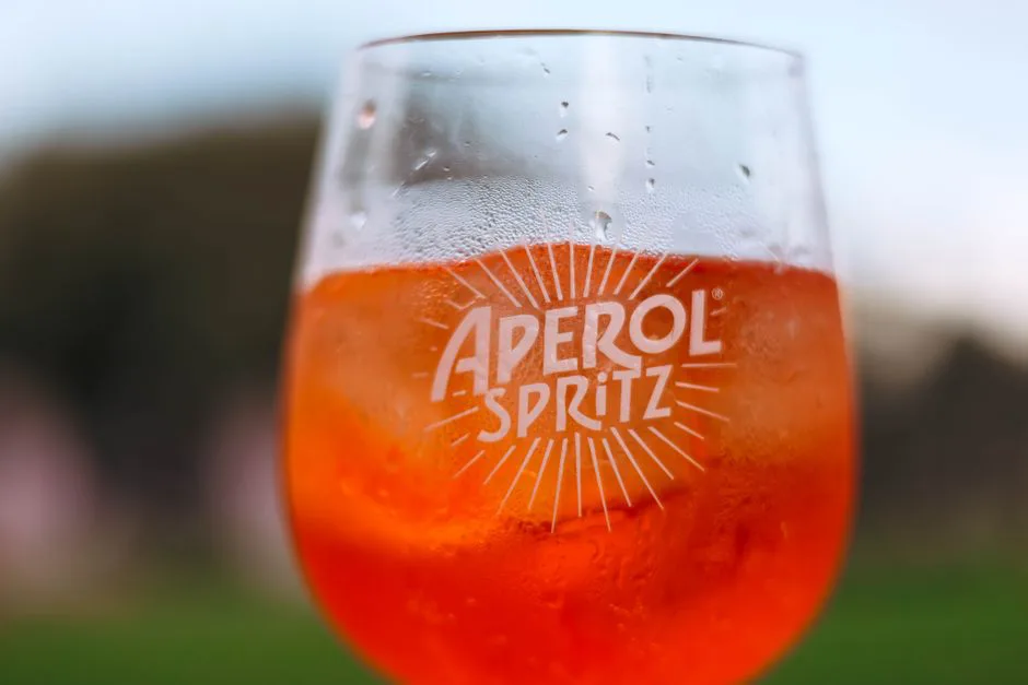 Refreshing Aperol Spritz cocktail on a sunny day with a blurred outdoor background.
