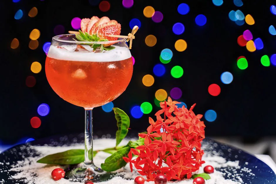 A vibrant strawberry cocktail garnished with fresh strawberries and red flowers, perfect for celebrations.