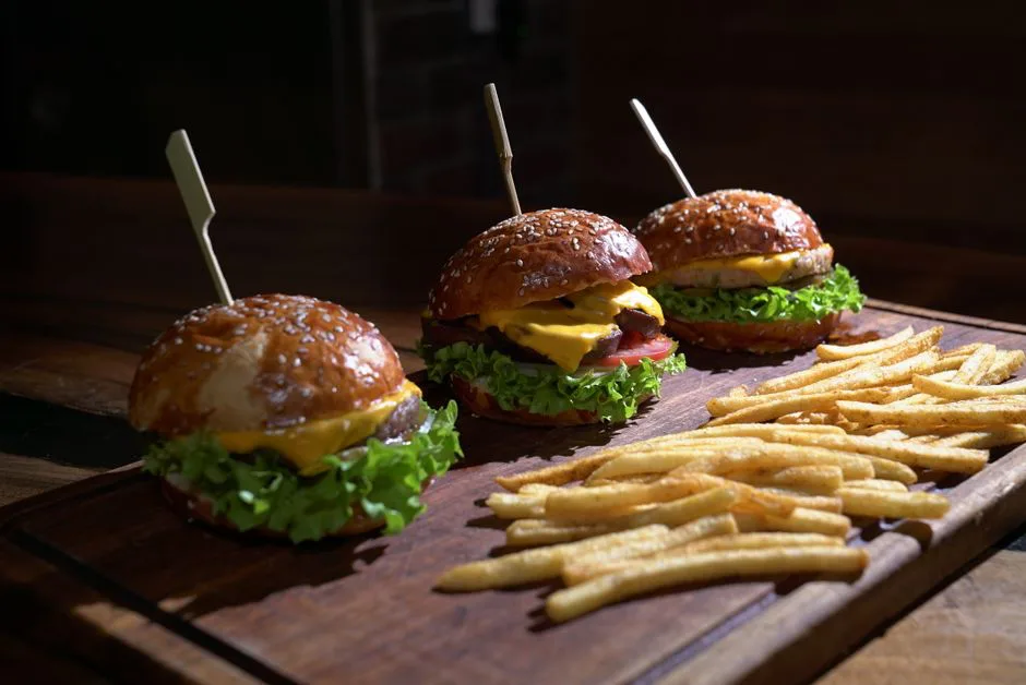 Three juicy cheeseburgers with lettuce, tomato, and fries on a wooden platter.