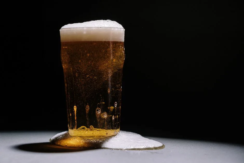 A studio shot of a frothy and overflowing pint of golden beer against a dark backdrop.