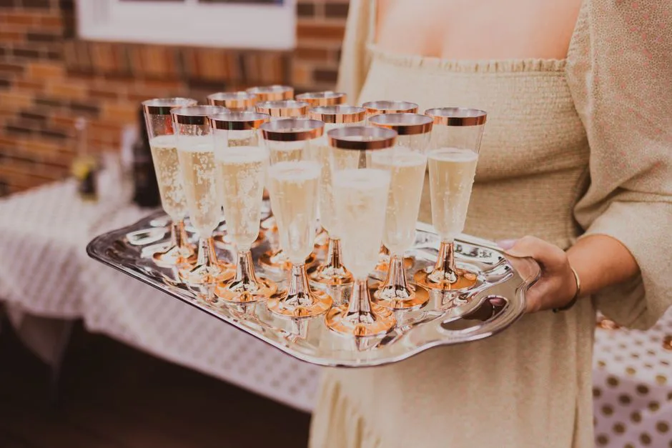 Crop anonymous female in elegant dress holding tray with glasses of champagne in banquet hall
