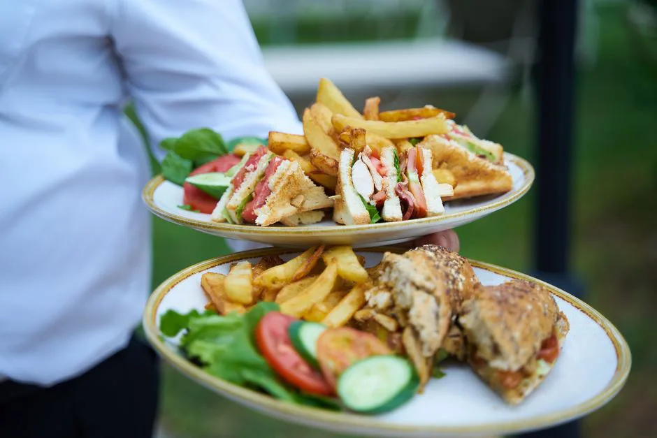Close-up of a waiter serving delicious sandwiches and fries on plates in an outdoor setting.