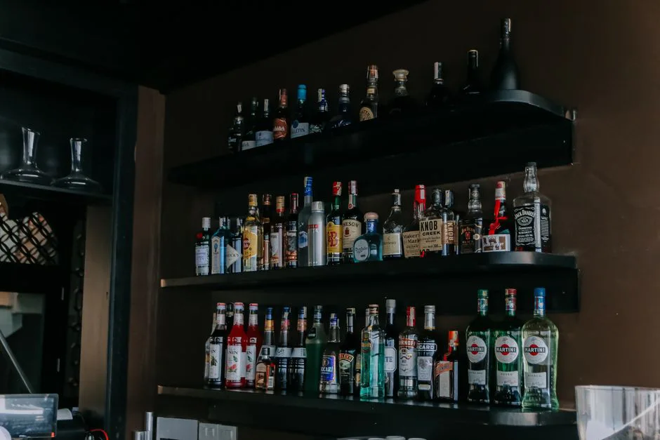 A modern bar with a wide selection of liquor bottles arranged on sleek black shelves.