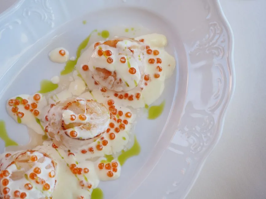 A close-up of a beautifully presented scallop dish garnished with creamy sauce and fish roe.