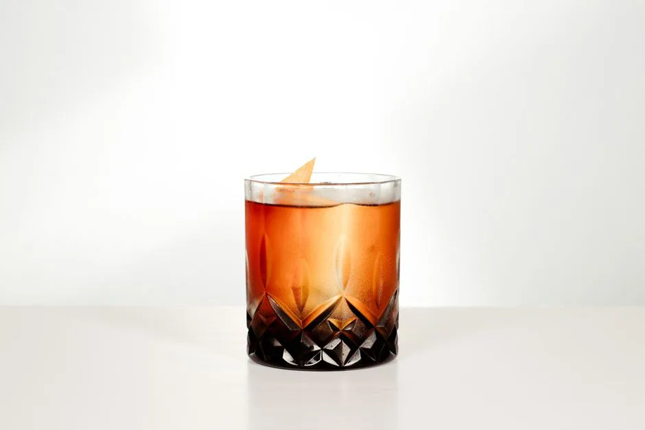 A sophisticated whiskey cocktail with an orange twist served in a crystal glass, perfect for a classy setting.
