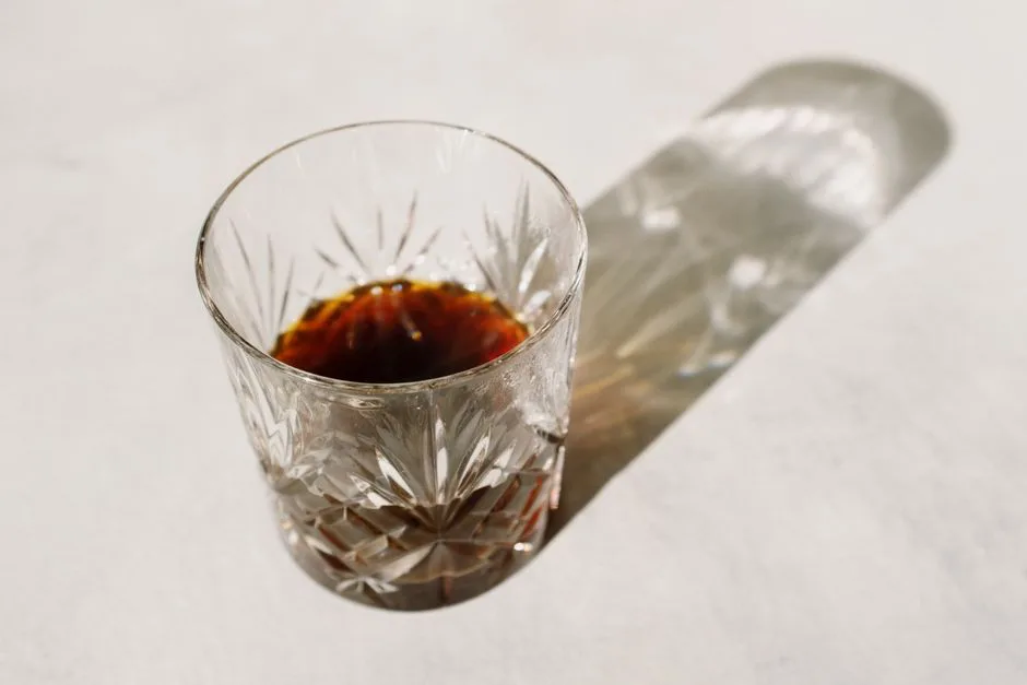 A crystal glass with dark liquor casting a shadow in warm sunlight.
