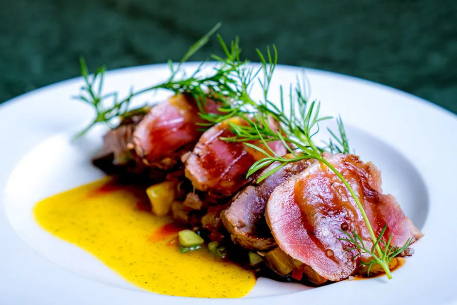 Close-up of gourmet seared tuna with a dill garnish served on a white plate.