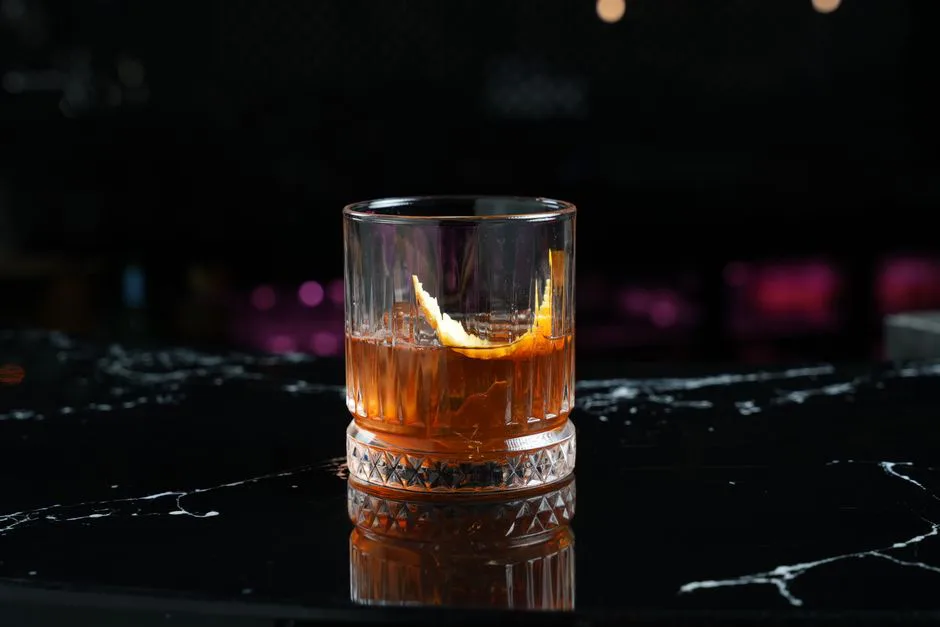 A cocktail glass with a citrus garnish sits on a polished black marble surface in a dimly lit setting.