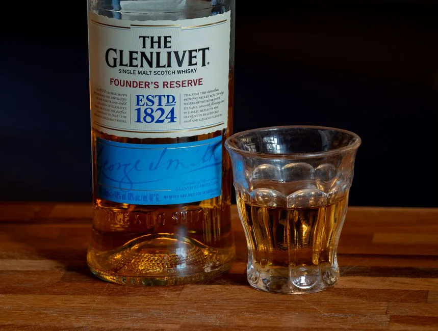 Close-up of The Glenlivet Founder’s Reserve whisky with a glass on a wooden surface.