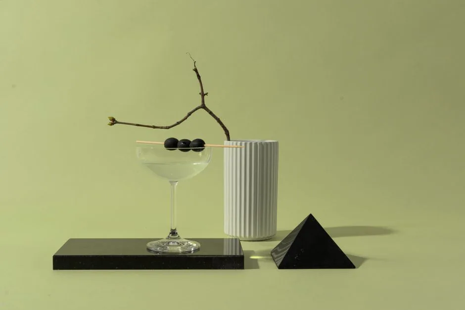 Stylized martini glass with olives, vase, and pyramid on a marble tray.
