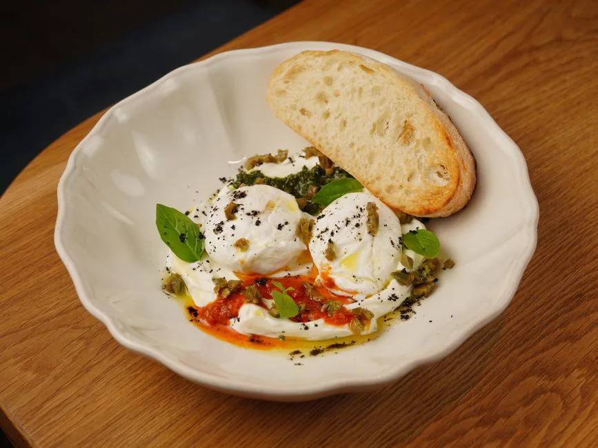 A delightful dish featuring fresh burrata cheese and basil served with a slice of rustic bread.