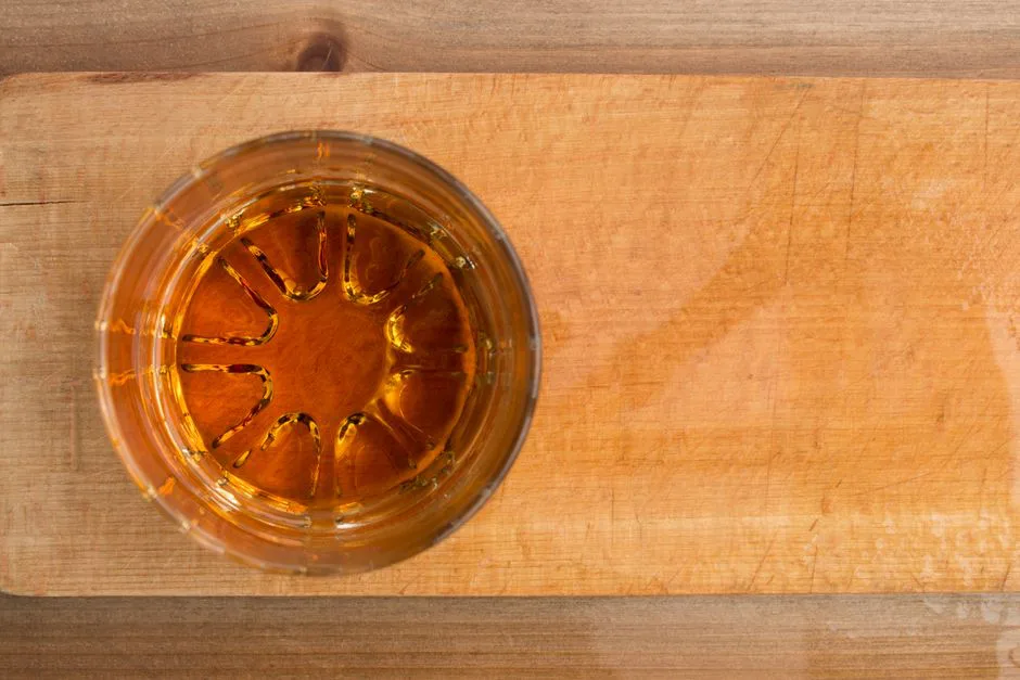 Aerial shot of amber whiskey in a glass on a wooden table, offering texture and warmth.
