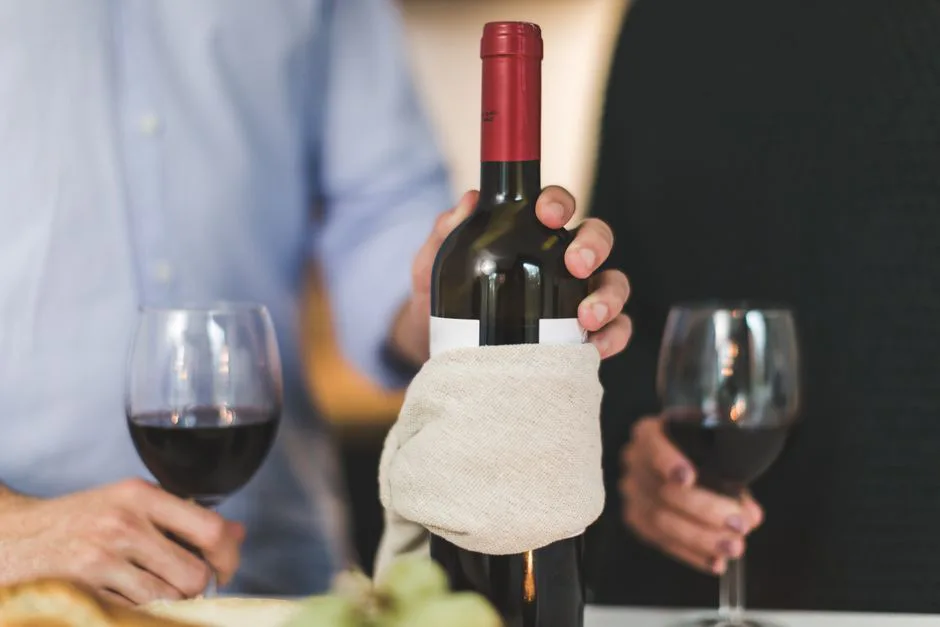 Two people enjoying red wine with a bottle wrapped in cloth, perfect for dining ambiance.