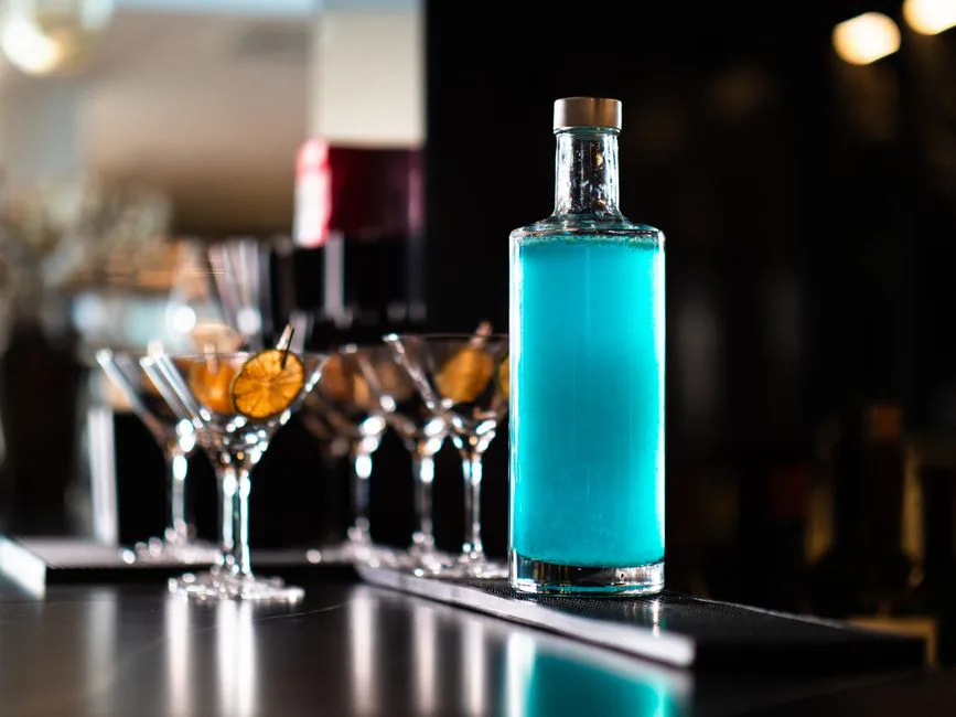Elegant display of a vibrant blue cocktail bottle with glasses, ideal for nightlife and bar themes.