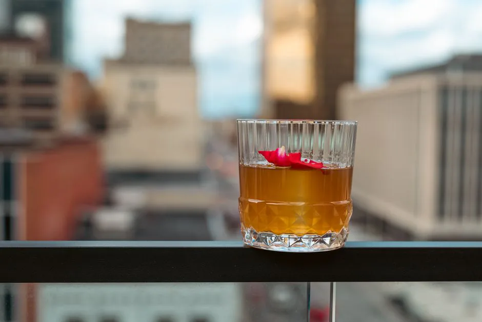 Glass of cocktail garnished with rose petal on a city balcony railing. Ideal for lifestyle or urban living themes.