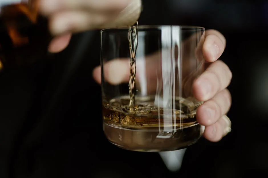 Hand pouring whiskey into a glass, capturing the rich texture and color of the beverage.