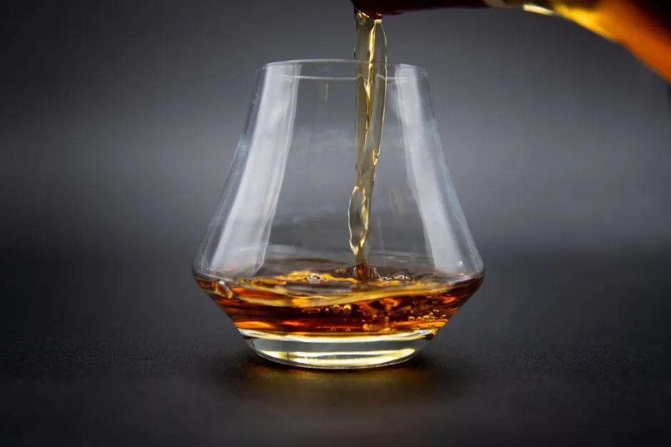 Aesthetic shot of whiskey being poured into a glass against a dark background.