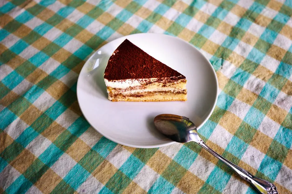 A tempting slice of tiramisu on a white plate with a silver spoon, perfect for dessert lovers.