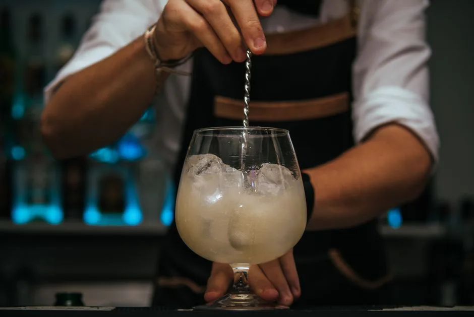 Close-up of bartender stirring a cocktail in a glass filled with ice.