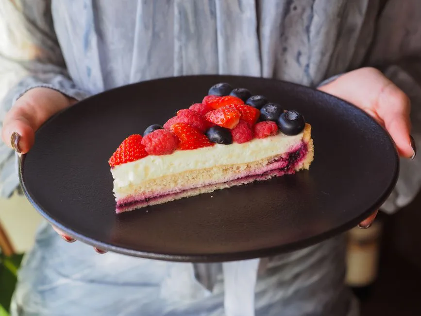 A close-up of a berry-topped cheesecake slice on a black plate, perfect for dessert lovers.