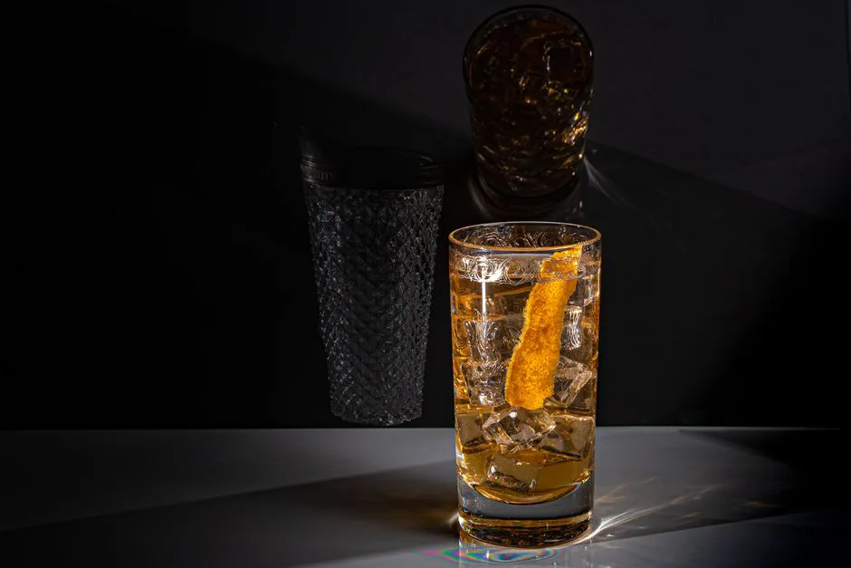 Glass of whiskey with lemon twist on a grey background. Perfect for cocktail themes.